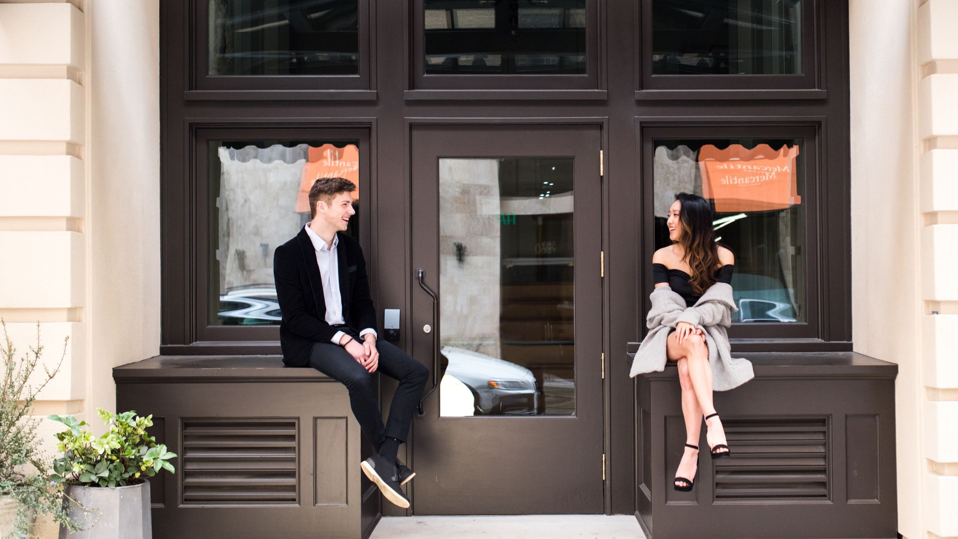 A Man And A Woman Sitting On A Bench In Front Of A Building