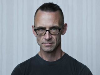 Chuck Palahniuk Standing In Front Of A Curtain
